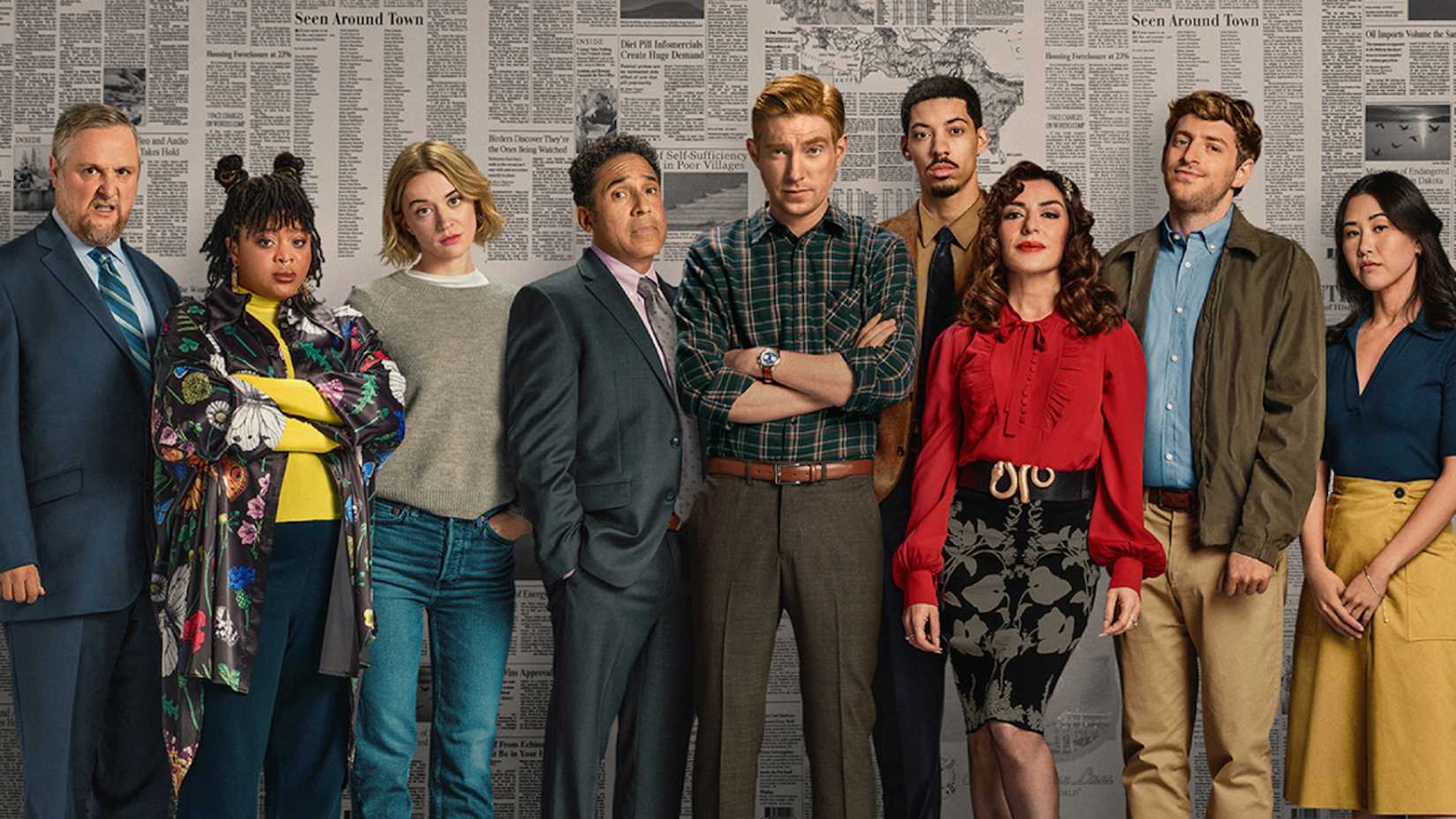 O elenco de The Paper da Peacock em frente a uma parede coberta de jornais.