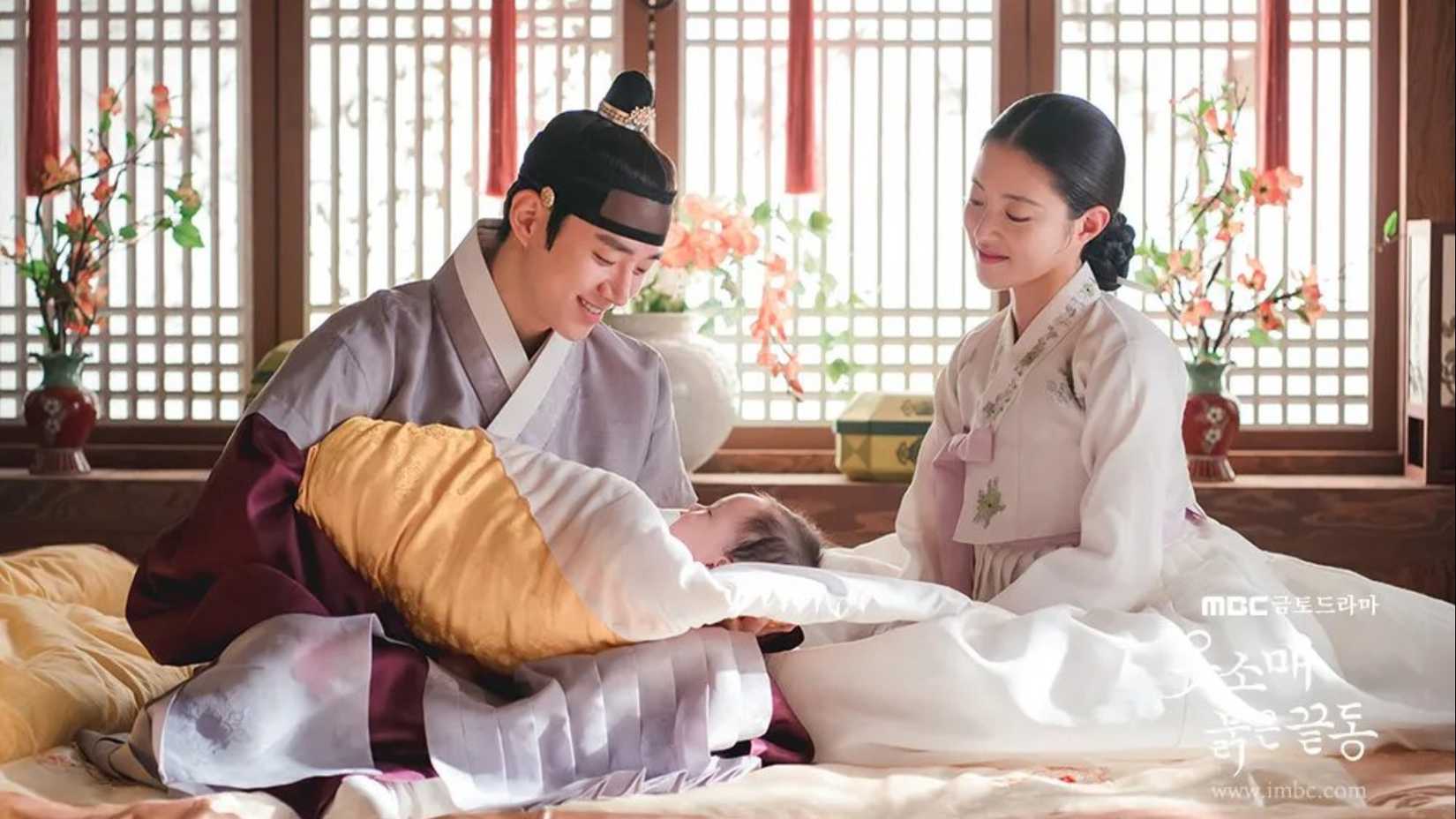 Um homem segurando um bebê enquanto uma mulher sorri em The Red Sleeve.