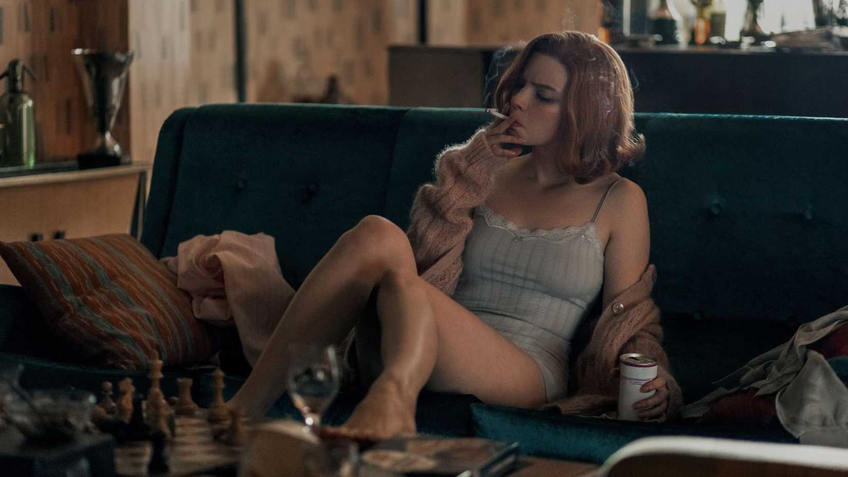 Beth Harmon fumando enquanto olha para um tabuleiro de xadrez em The Queen's Gambit.