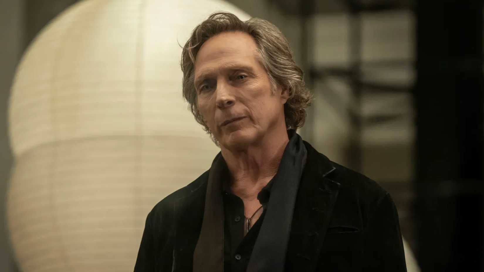 William Fitchner as Jasper with his head cocked wearing a sly smile in Talamasca The Secret Order