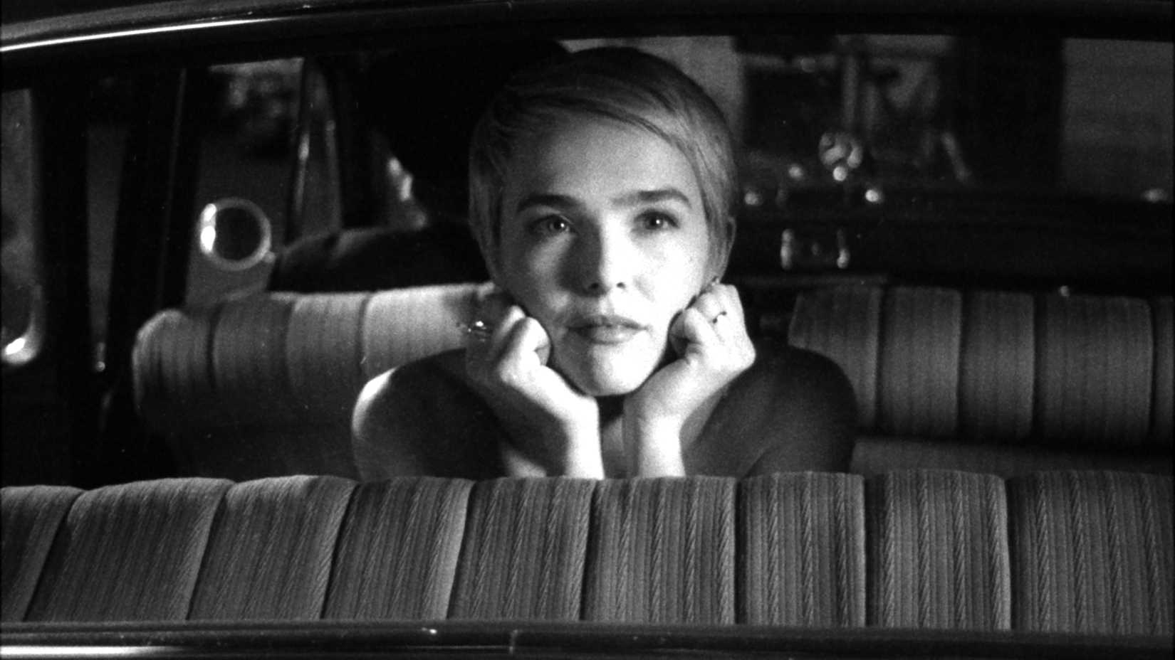 Zoey Deutch als Jean Seberg, das Kinn gedankenverloren in einem Auto in Nouvelle Vague