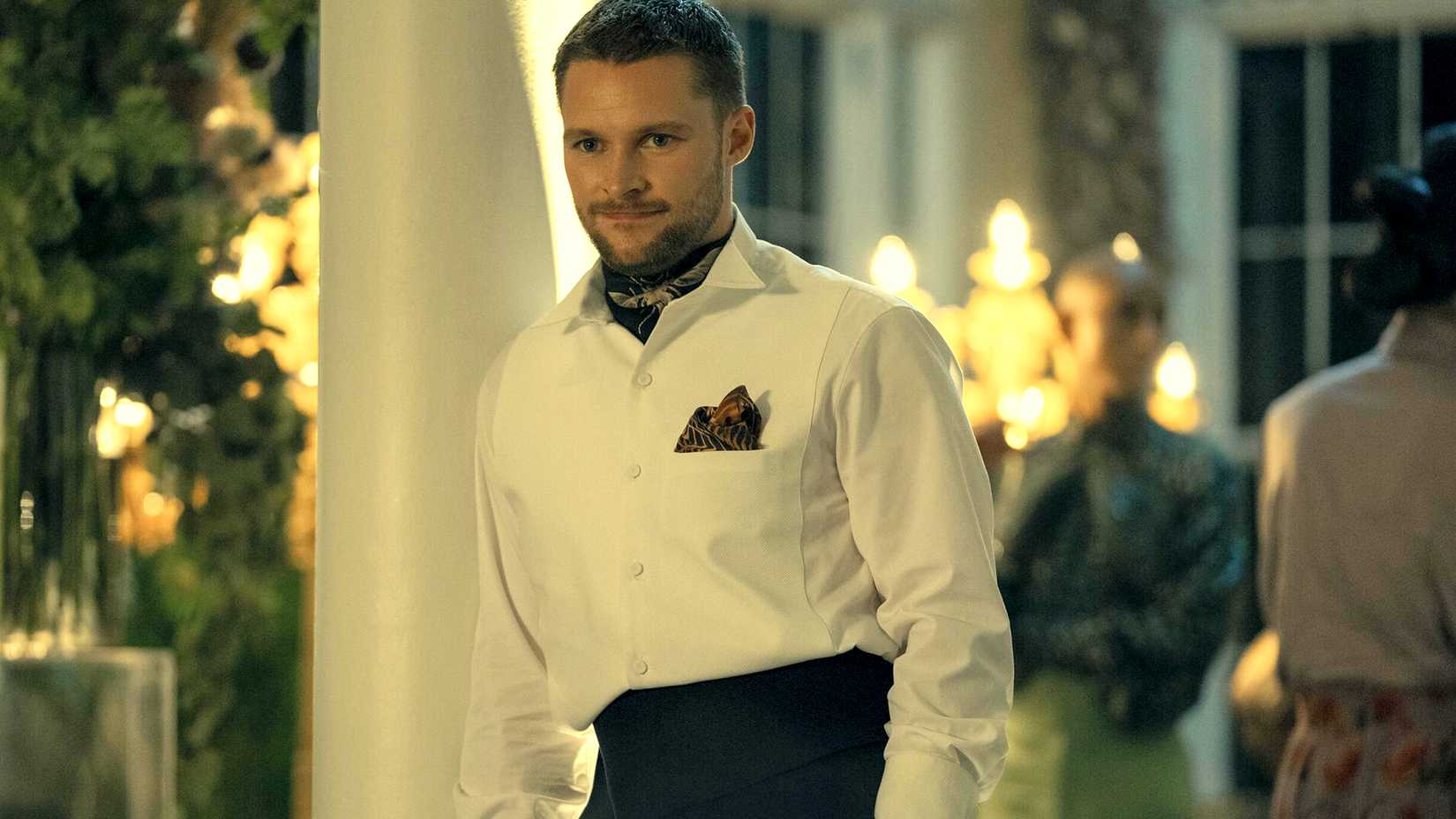 Jack Reynor as Burton Fisher wears a suit and smiles at a lavish venue in Prime Video's