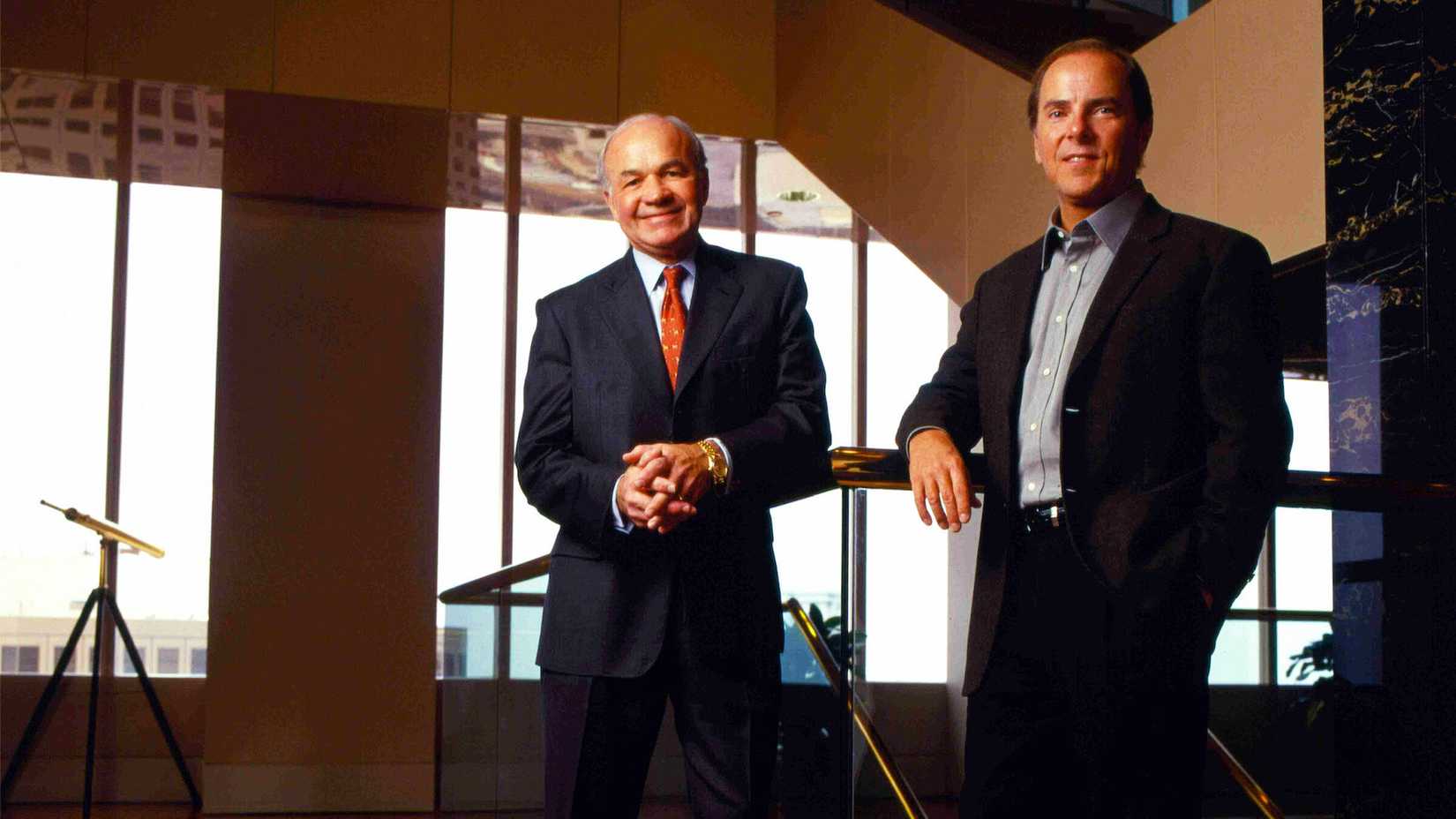 Two men in businesswear smile at a camera.