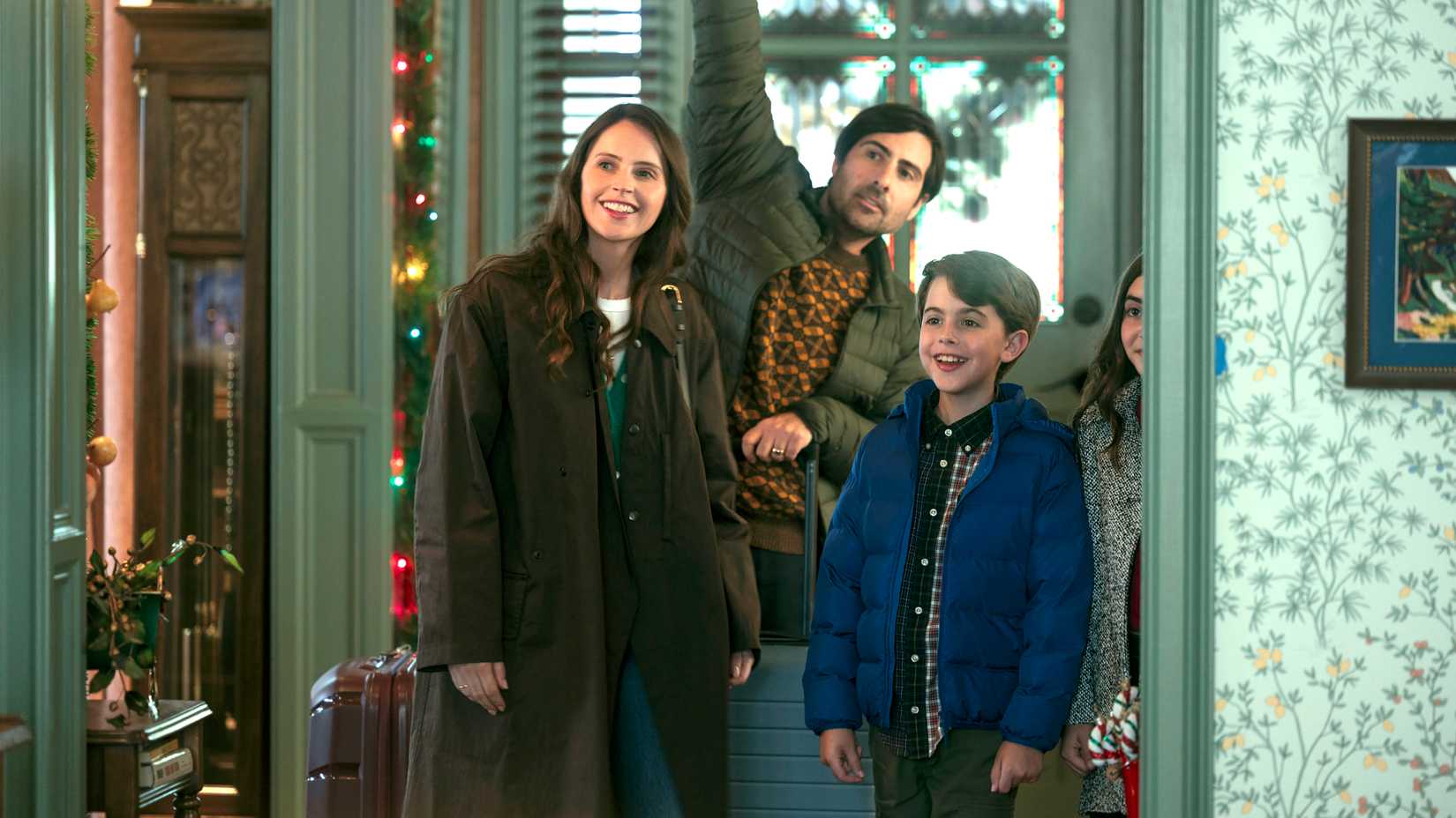 Felicity Jones, Jason Schwartzman and a couple of kids smiling and standing in a foyer in Oh. What. Fun