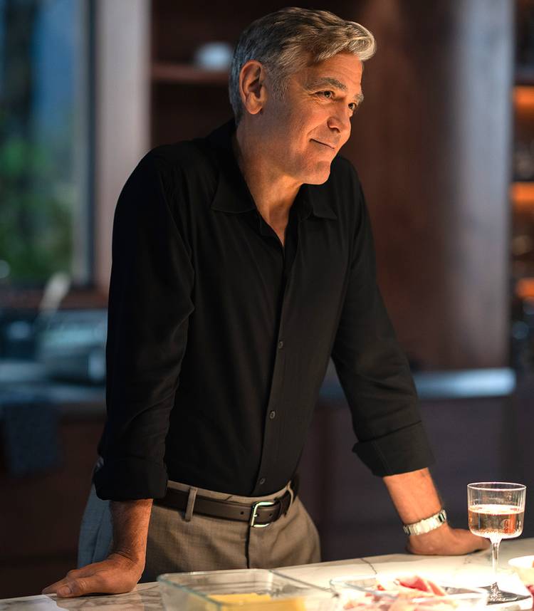 george clooney s jay smiling and leaning against a counter in jay kelly