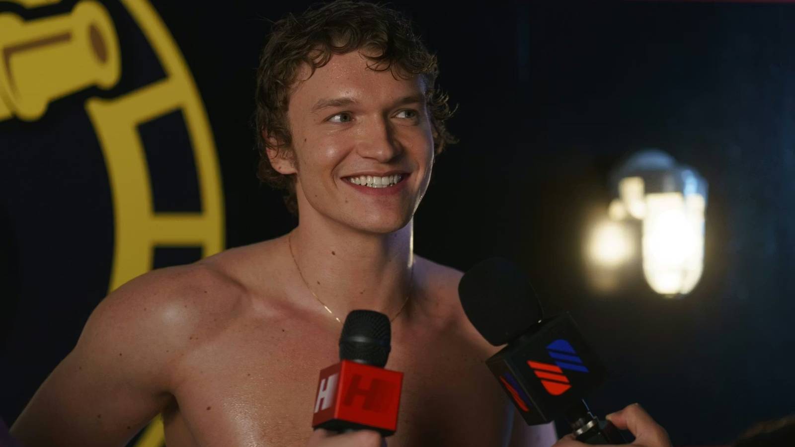 Heated Rivalry still featuring Ilya Rozanov smiling to cameras with microphones held out to him.