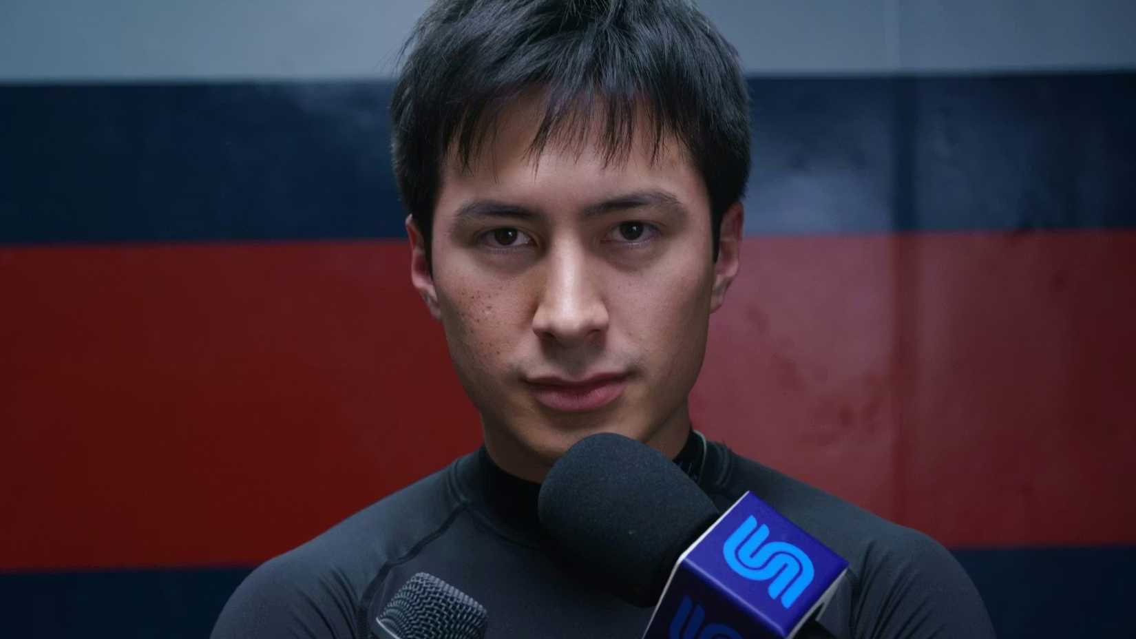 Heated Rivalry still featuring Shane Hollander smiling to camera and speaking into a microphone.