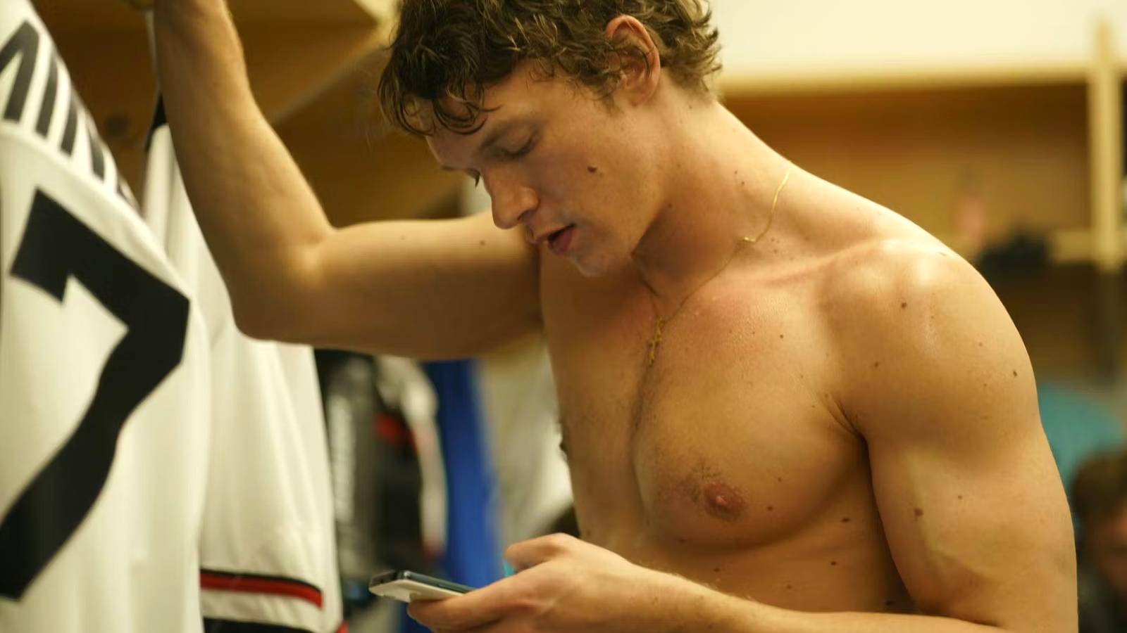 Ilya Rozanov looks at his phone while shirtless in Heated Rivalry
