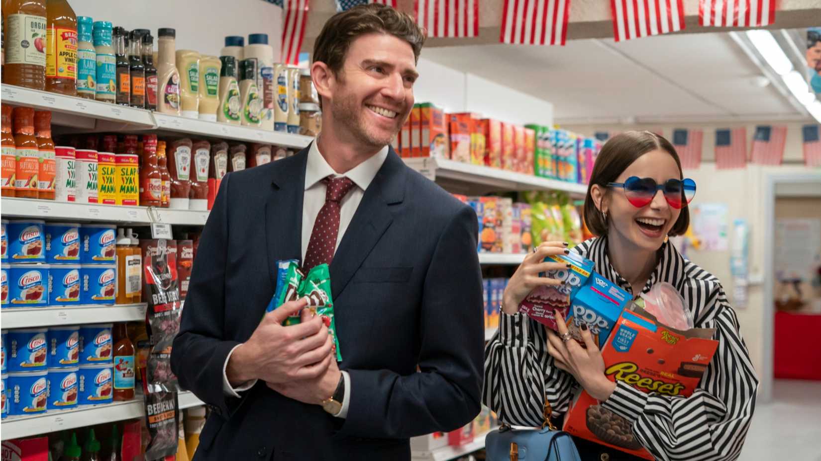 Jake and Emily smiling at the U.S. Embassy's American snack supply in Emily in Paris