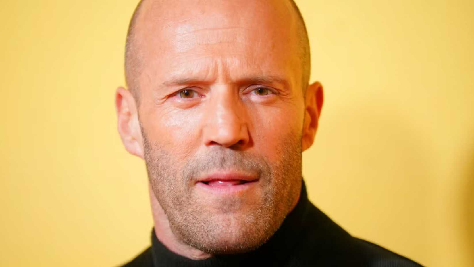 Jason Statham posed in front of a yellow wall