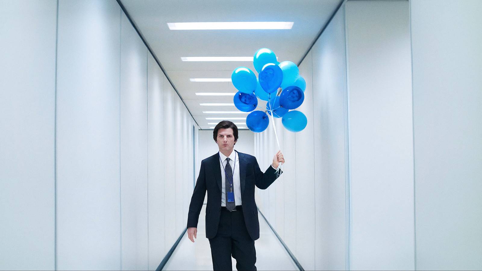 Mark (Adam Scott) holding a string of blue balloons in a white hallway in Severance