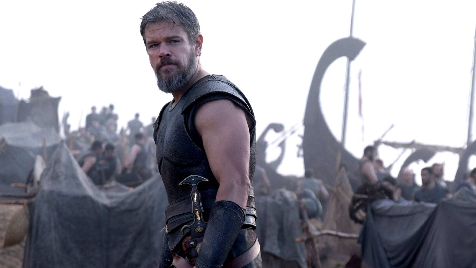 Matt Damon as Odysseus looking off the left with a ship and crew behind him in The Odyssey
