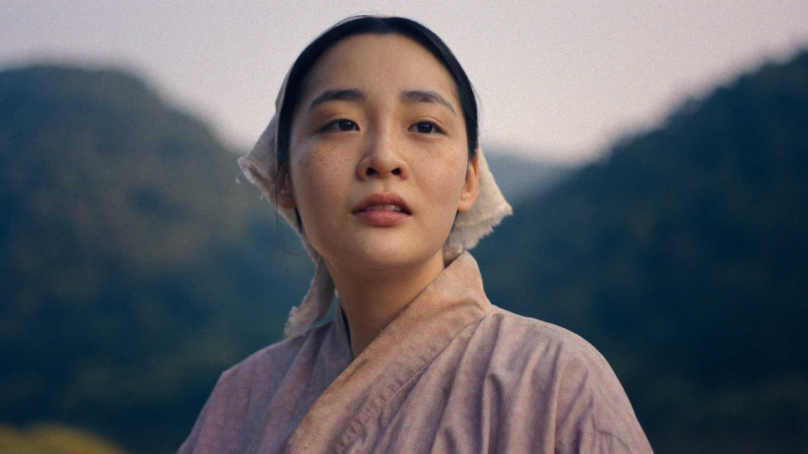 A woman stands in front of mountains in the K-drama Pachinko.