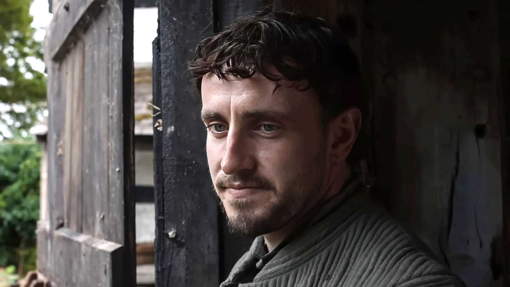 Paul Mescal as William smiling while standing in a doorway in Hamnet