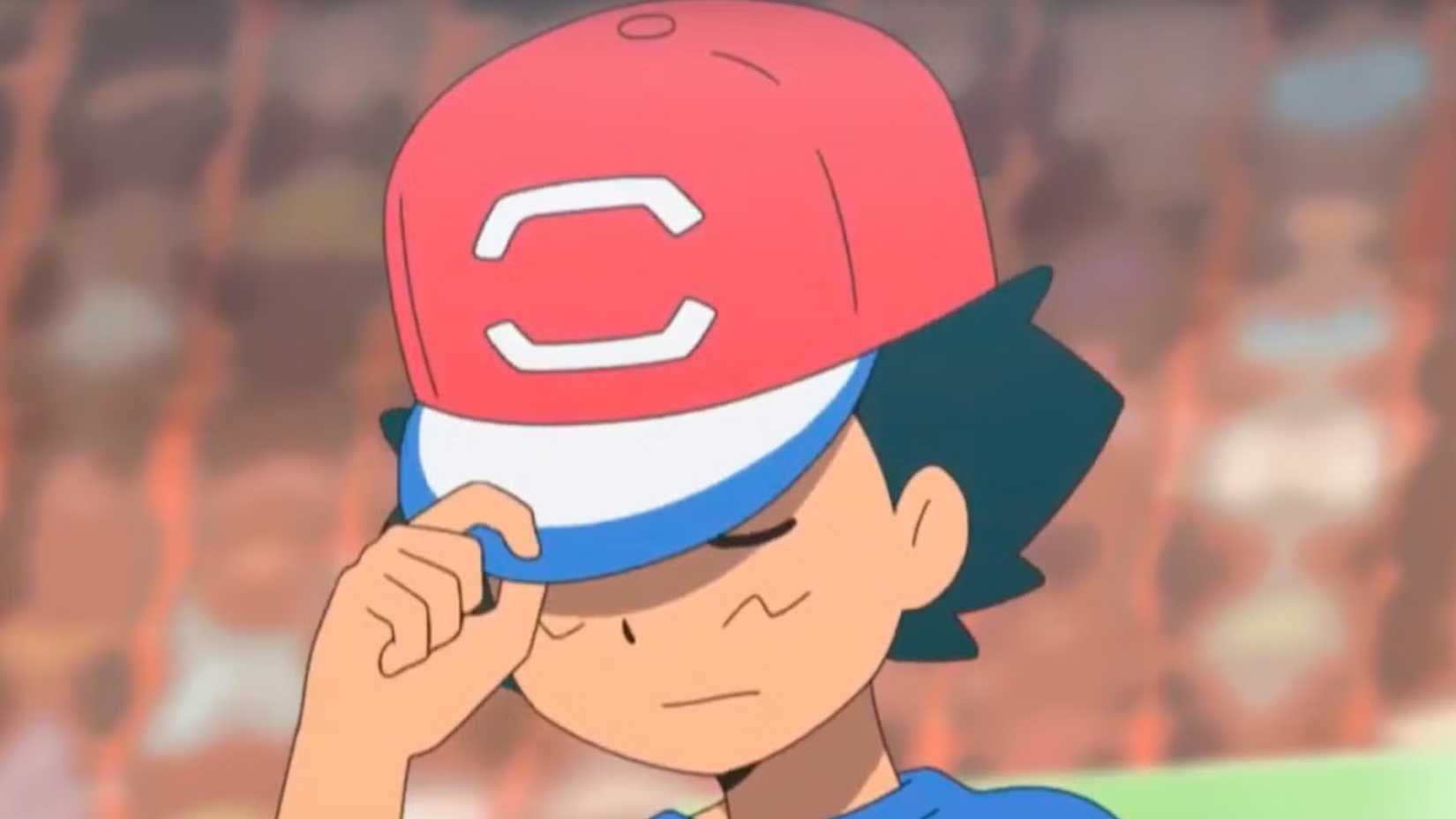 Pokémon's Ash holding his cap over his eyes and looking solemn.