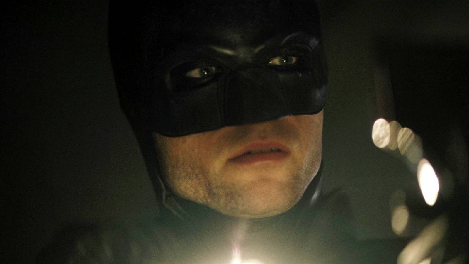 Robert Pattinson's Batman with a flashlight from below the frame and investigating in The Batman