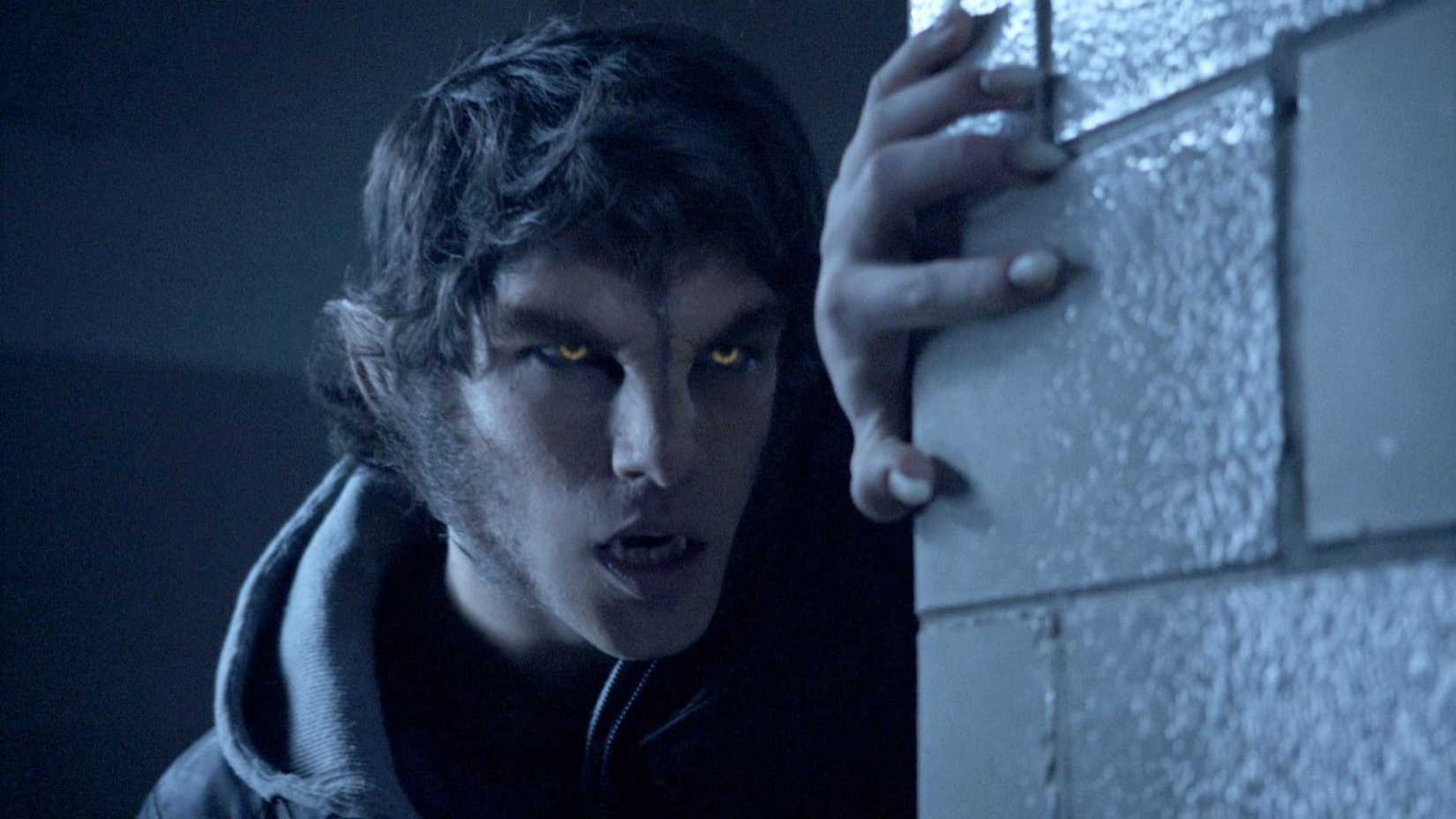 Tyler Posey espiando por uma parede como o lobisomem Scott McCall em Teen Wolf.