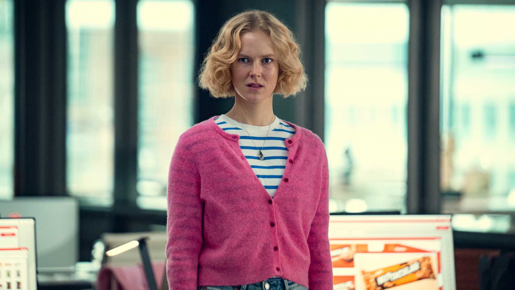 A woman in a pink sweater looks disgusted in an office in Black Mirror.