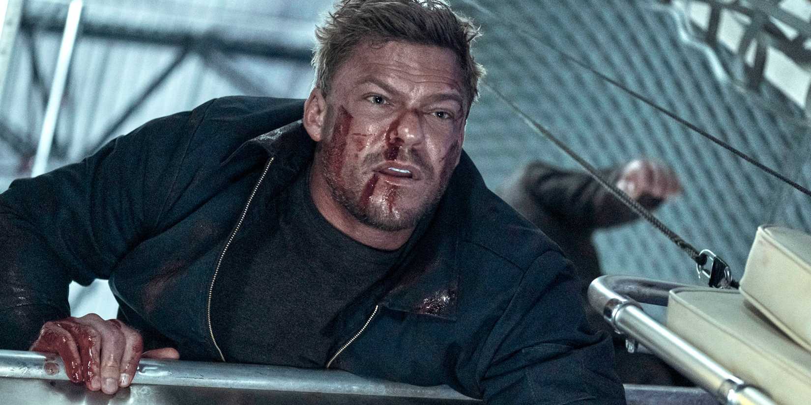 Alan Ritchson looking out of an open plane in Reacher