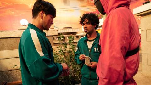 Ali (Anapum Tripathi) and Sang-woo (Park Hae-soo) playing marbles as a guard watches in Squid Game season 1, episode 6
