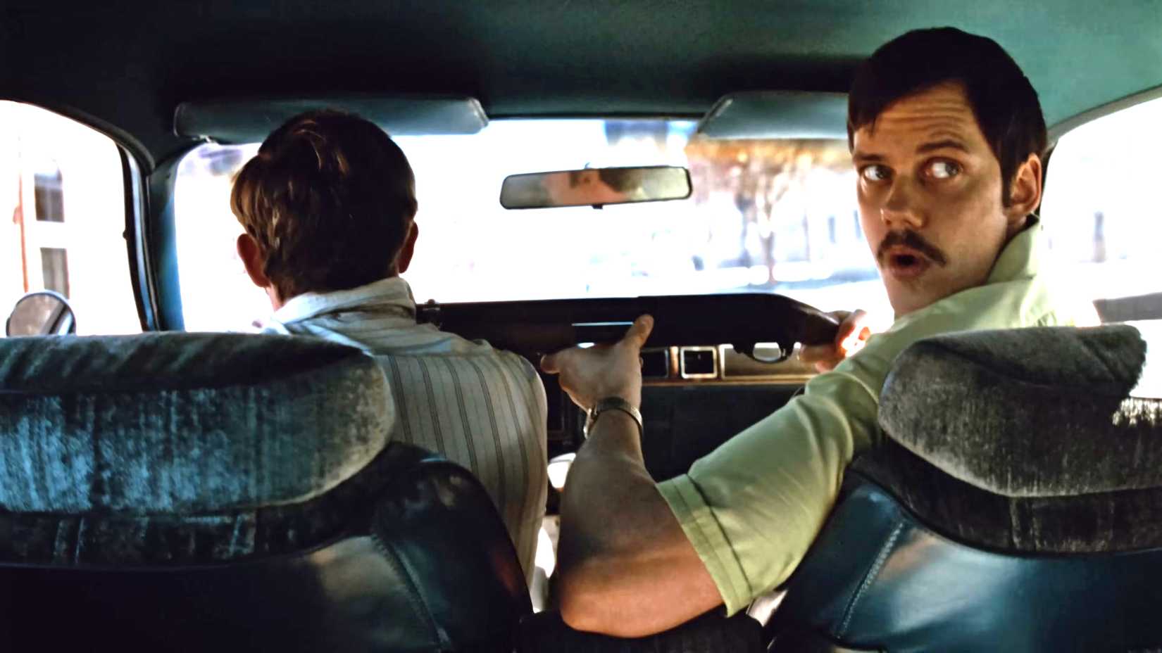 Bill Skarsgård's Tony looking over his shoulder while aiming the shotgun at Dacre Montgomery's Richard as he drives in Dead Man's Wire