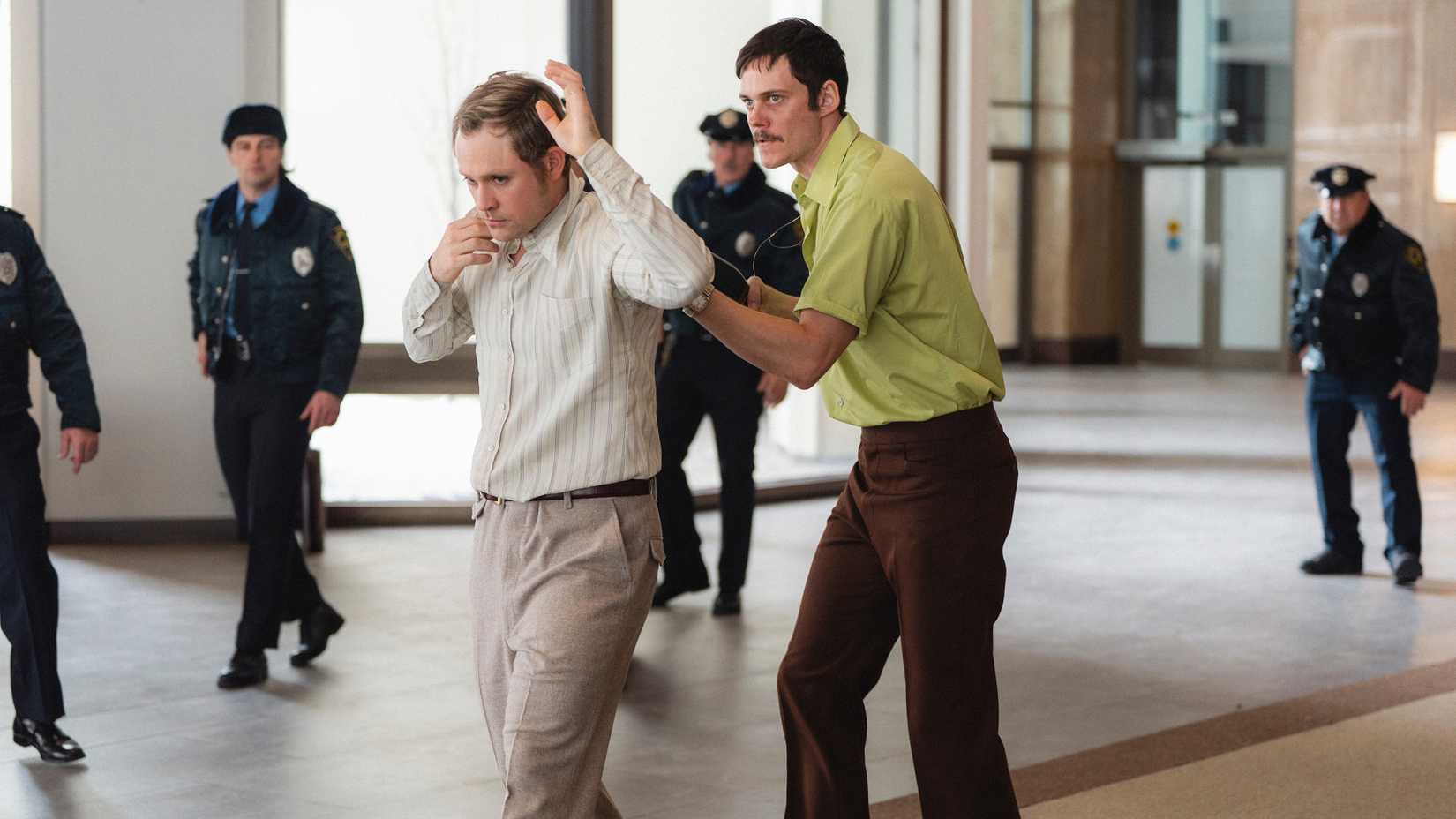 Bill Skarsgård's Tony walking Dacre Montgomery's Richard through the lobby with police around them in Dead Man's Wire