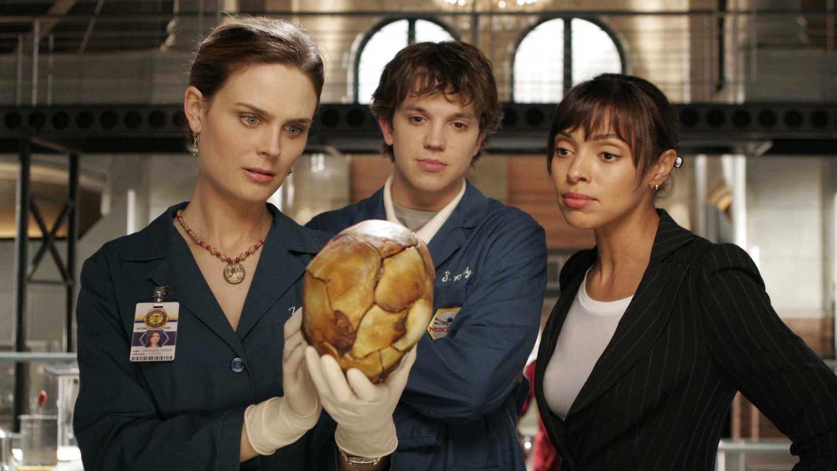 Três pessoas olhando para um crânio em Bones, temporada 2, episódio 1.