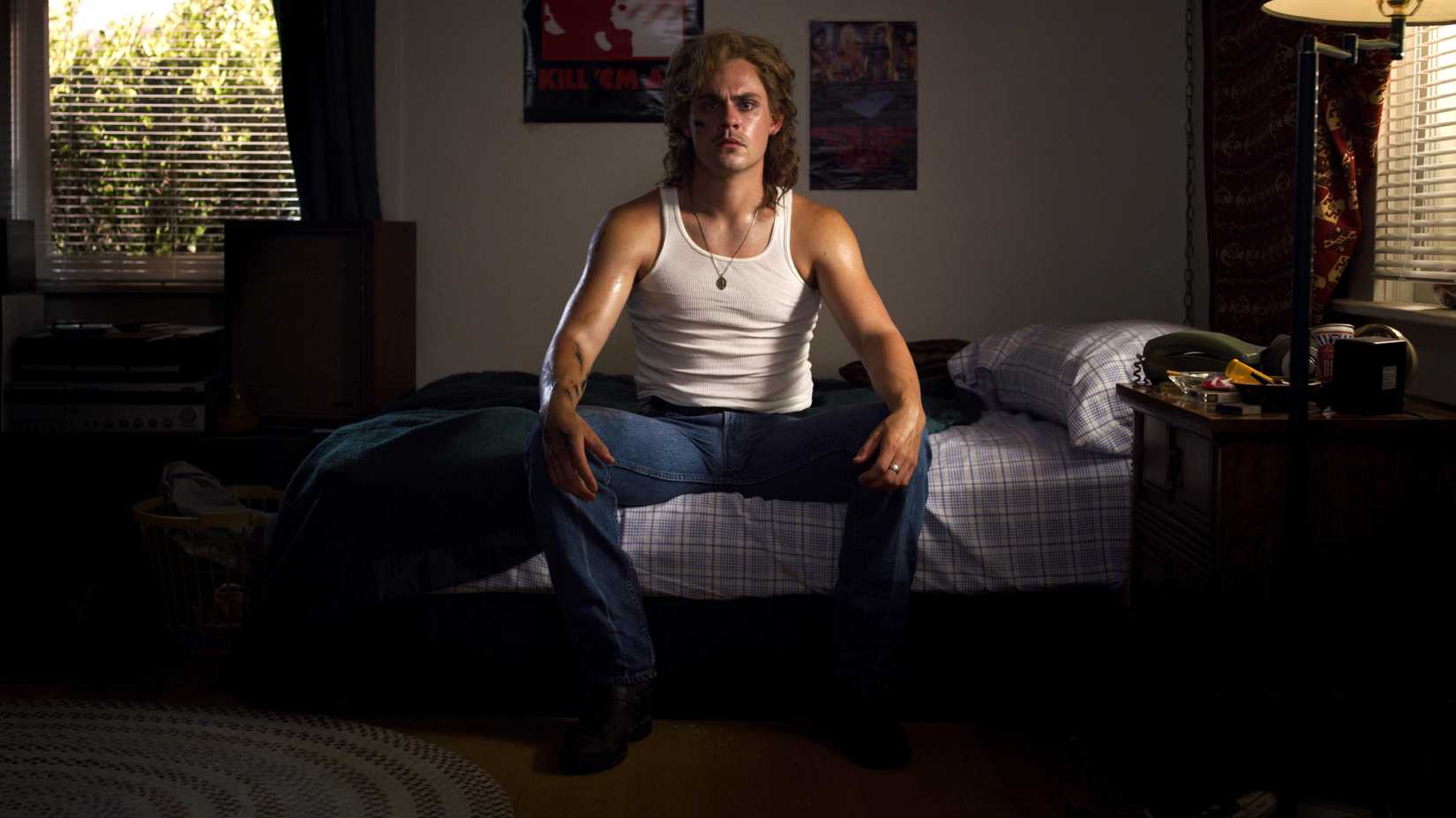 Dacre Montgomery sitting on a bed as Billy in Stranger Things season 3