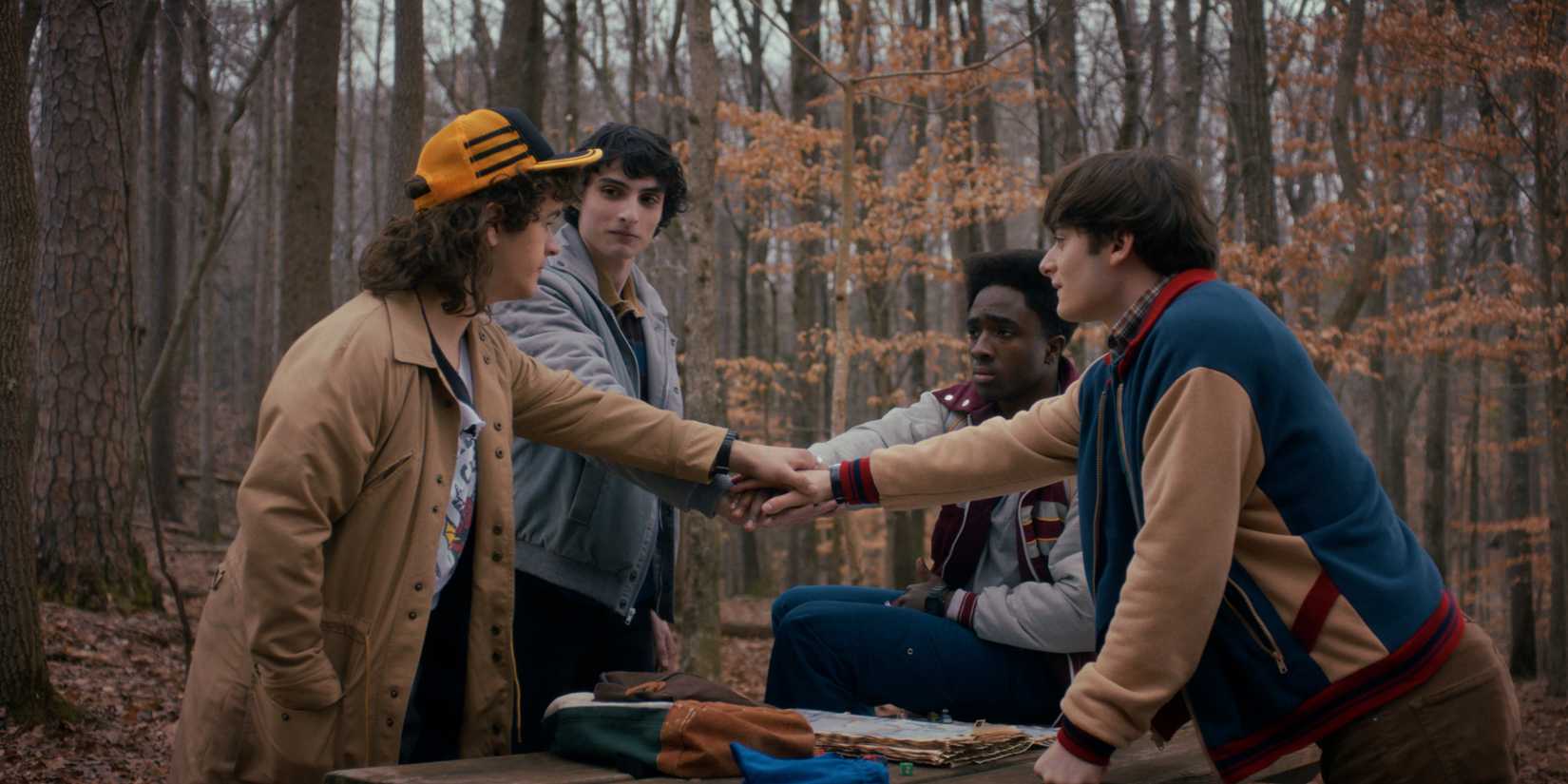 Dustin, Mike, Lucas e Will juntando as mãos em círculo em Stranger Things temporada 5