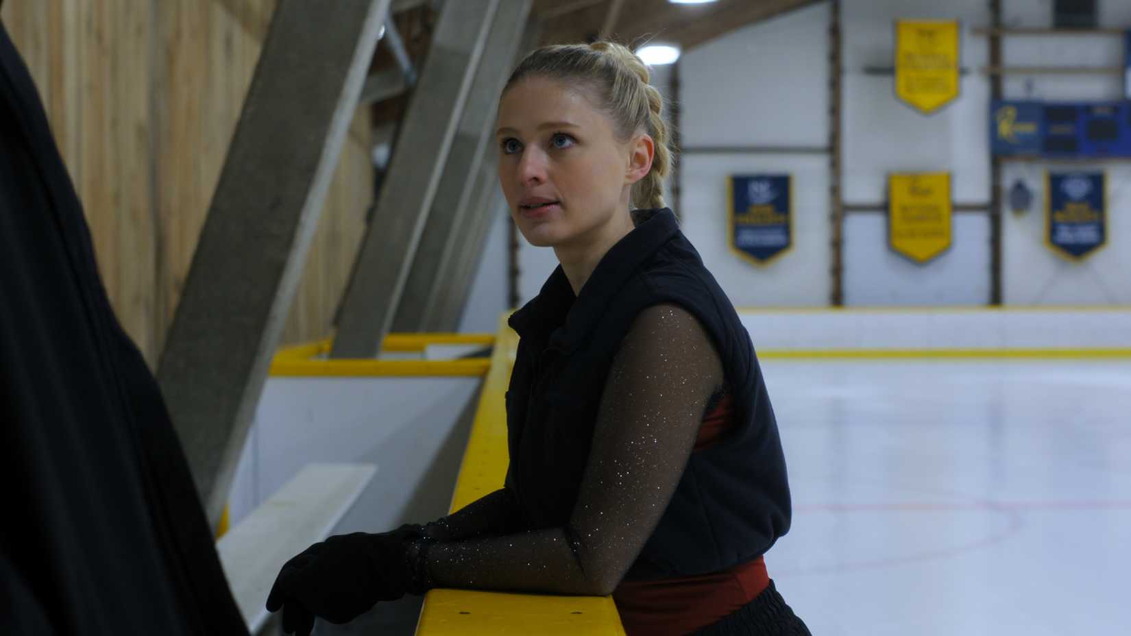 Elise leans on the edge of the ice rink in Finding Her Edge