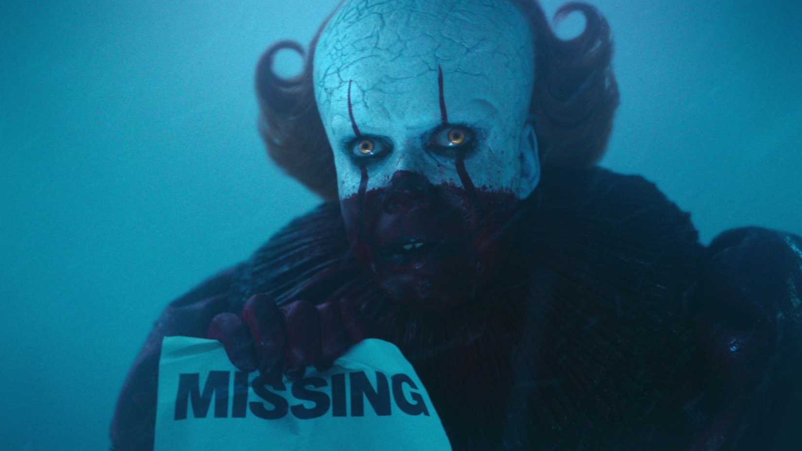 Pennywise (Bill Skarsgård) covered in blood and holding up a missing child poster in It: Welcome to Derry.
