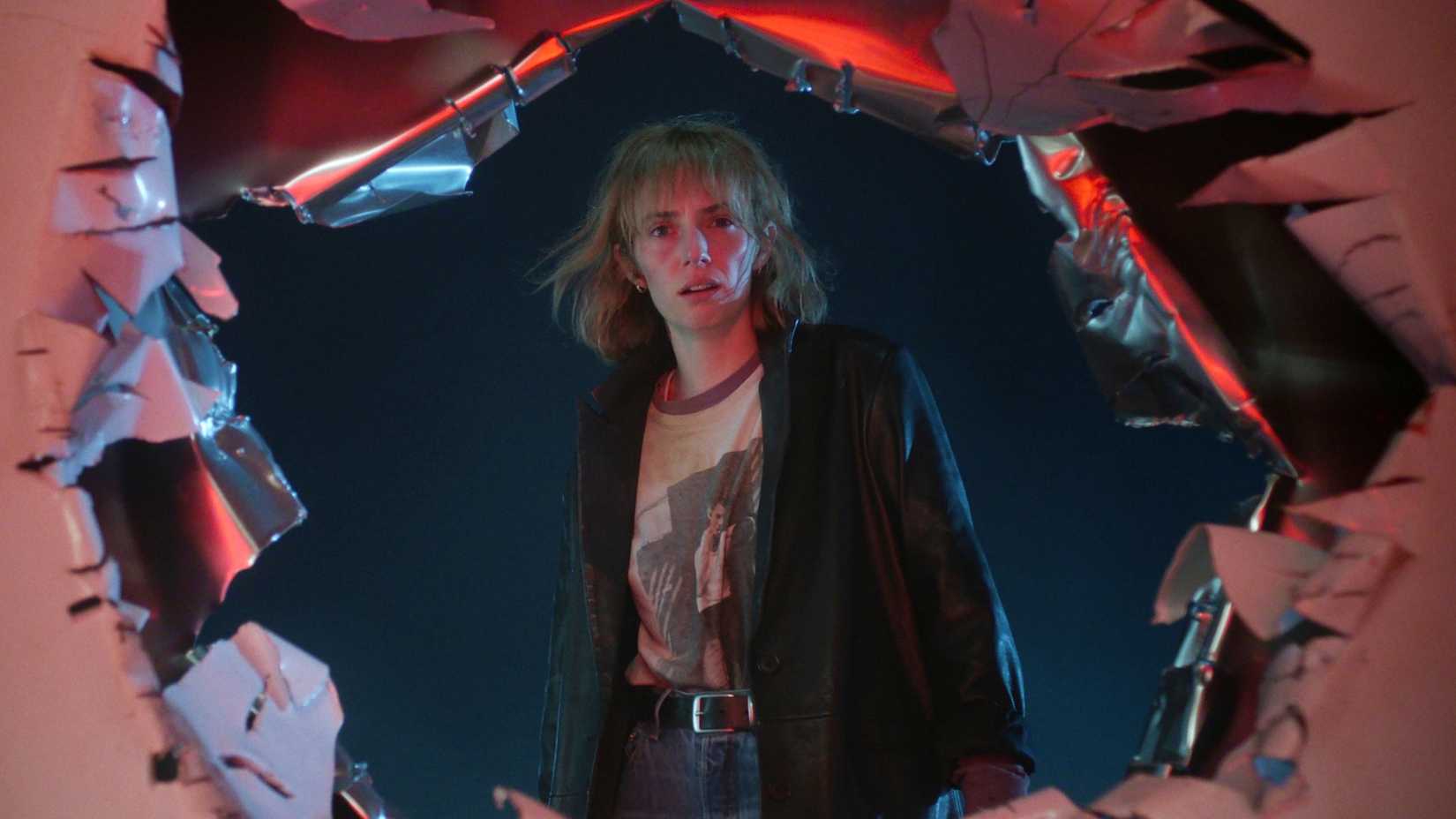 Maya Hawke's Robin stares through a hole in a metal wall in Stranger Things season 5