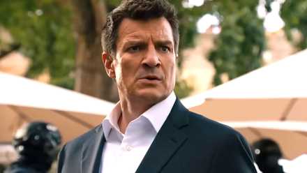 Nolan de Nathan Fillion con un traje mirando intensamente con hombres con equipo táctico detrás de él en la temporada 8 de The Rookie