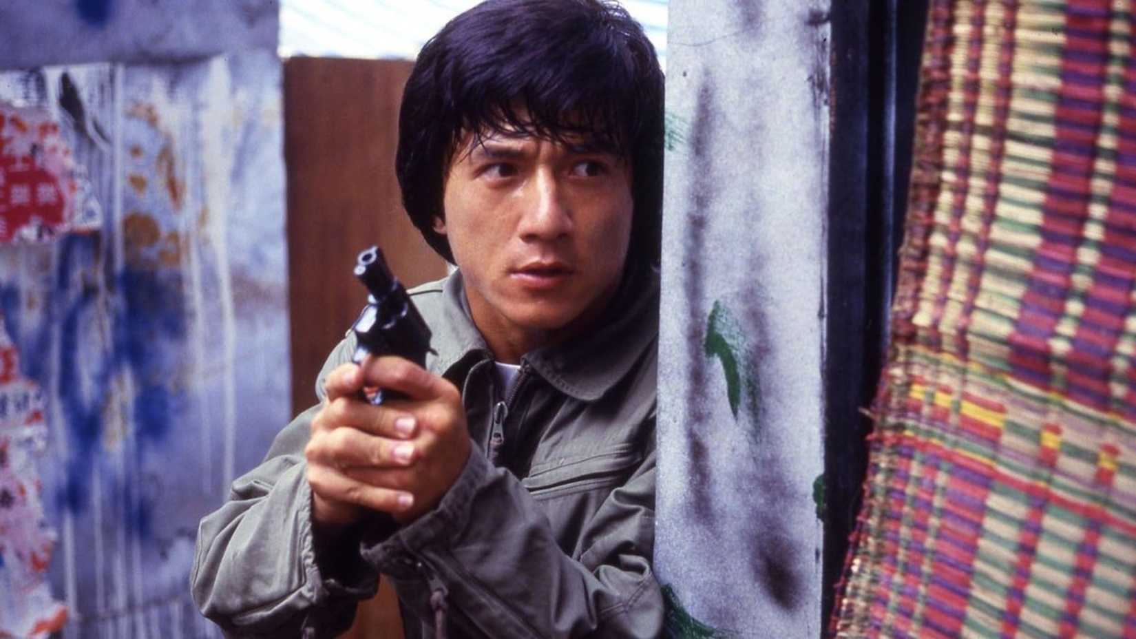 Jackie Chan holds a pistol while looking around a corner in Police Story