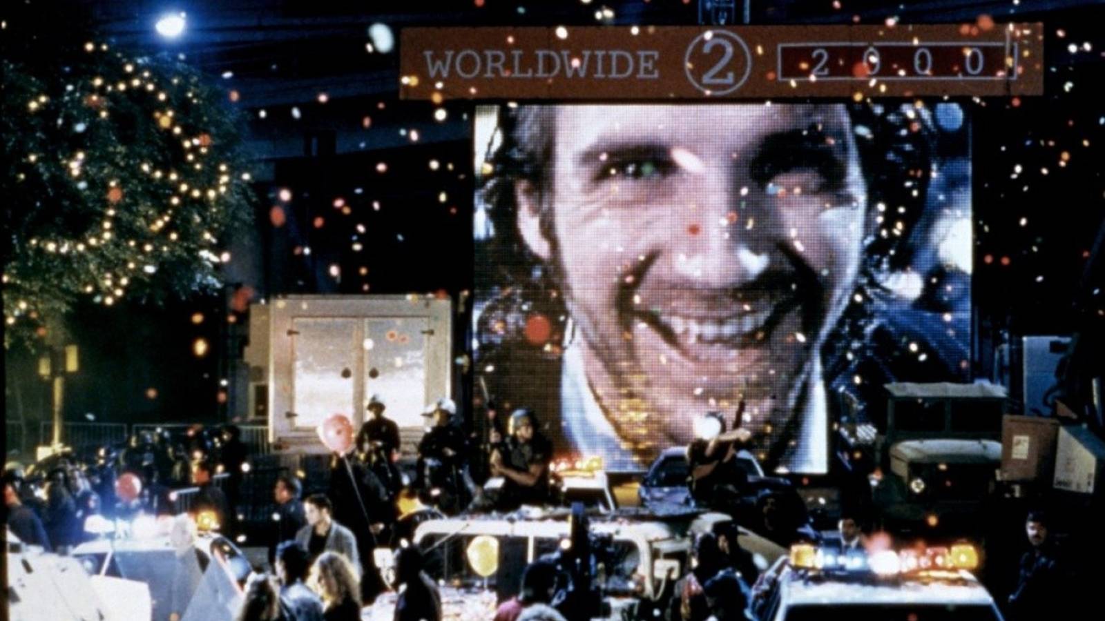 Ralph Fiennes appears on a large screen at a new years celebration in Strange Days