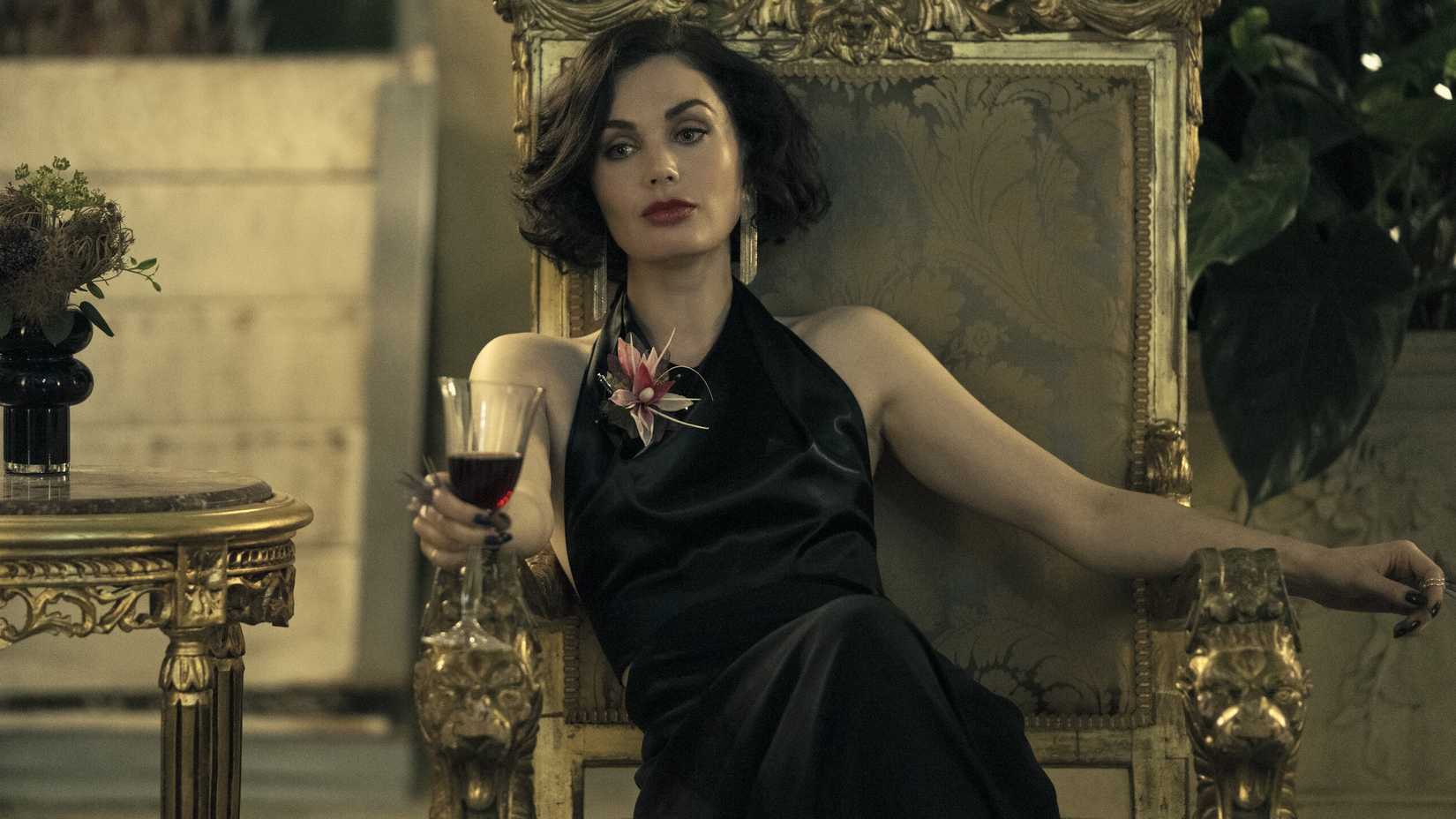 Poppy Corby-Tuech als Mariel Raphael sitzt in einem Stuhl und hält ein Glas Wein in der Hand in „The Peripheral“.