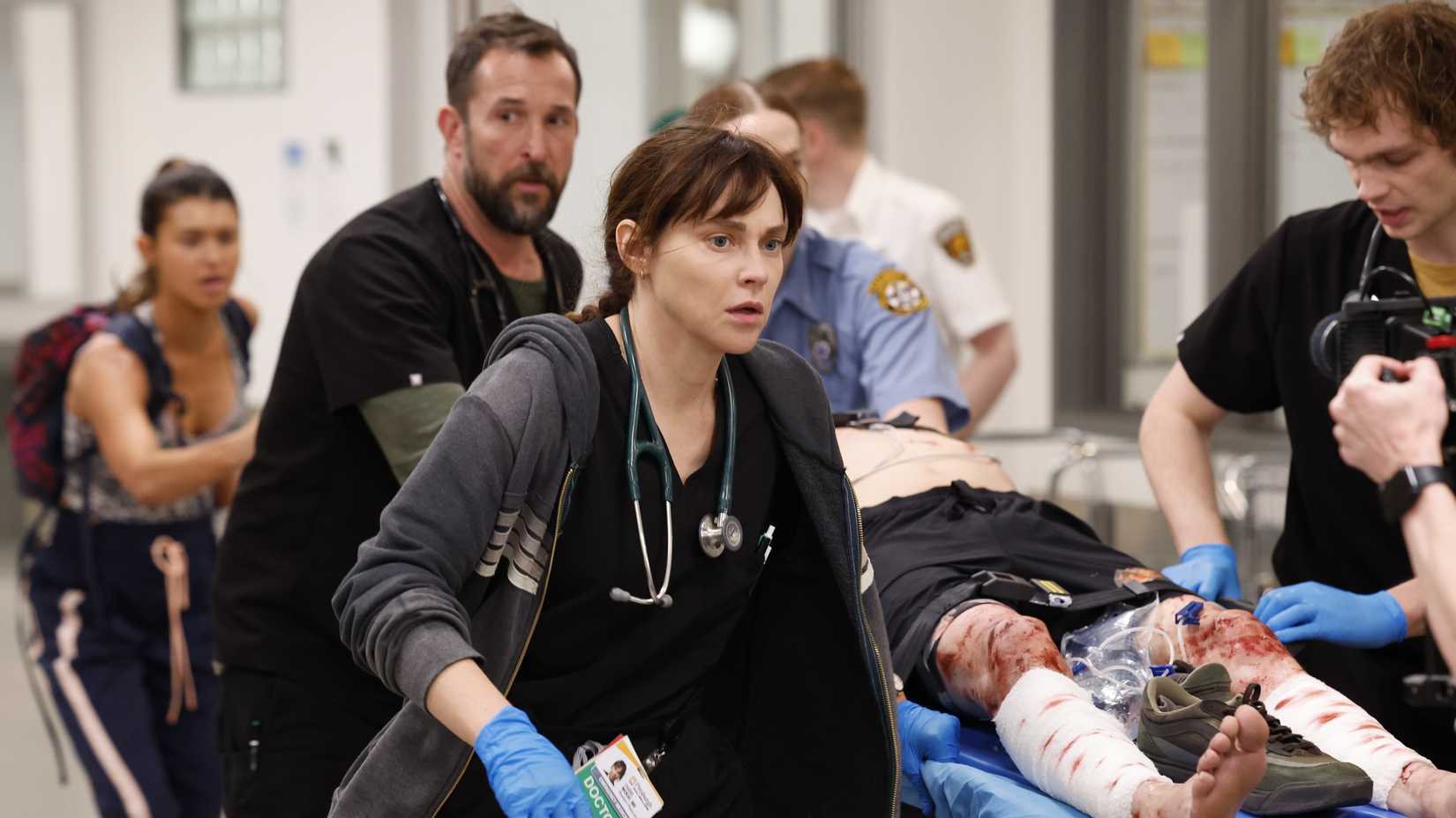 Dr. Robby (Noah Wyle) e Dra. McKay (Fiona Dourif) caminham ao lado de um paciente em maca na 2ª temporada de The Pitt.