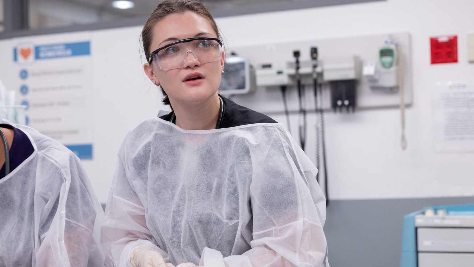 Isa Briones as Dr. Trinity Santos staring at something in an emergency room in The Pitt.