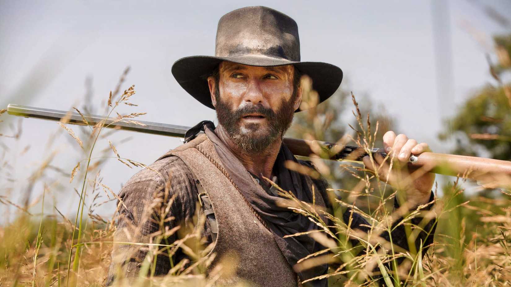 Tim McGraw as James Dutton holding a rifle in a field in 1883