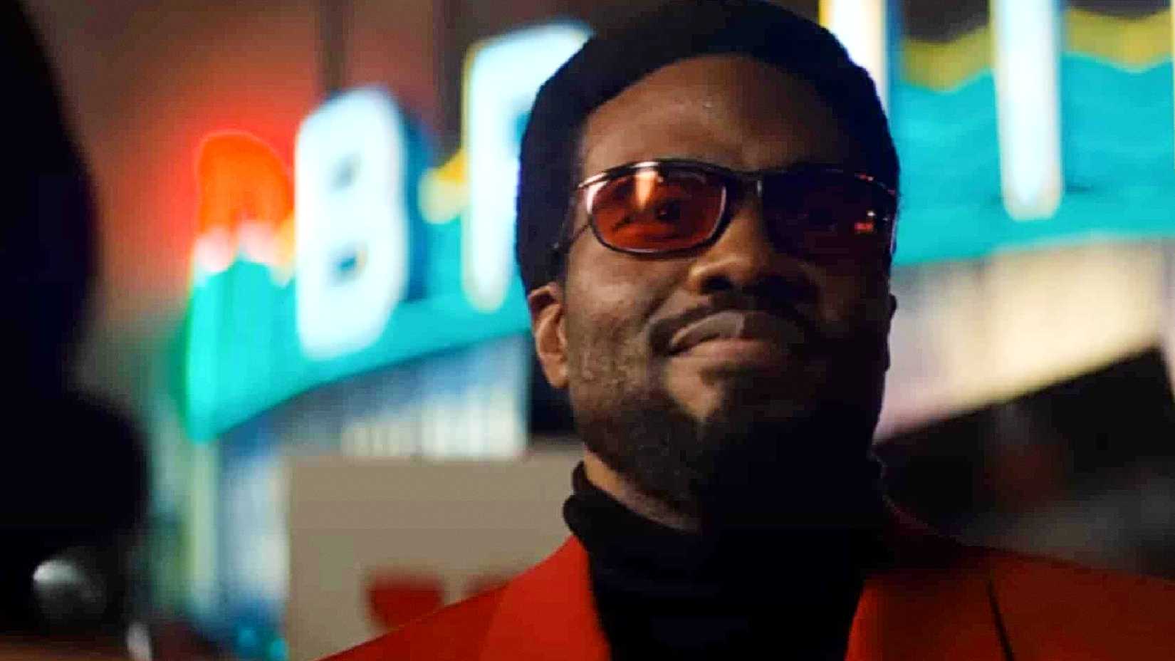 Yahya Abdul Mateen III's Simon Williams smiles wearing his red jacket and glasses in Wonder Man