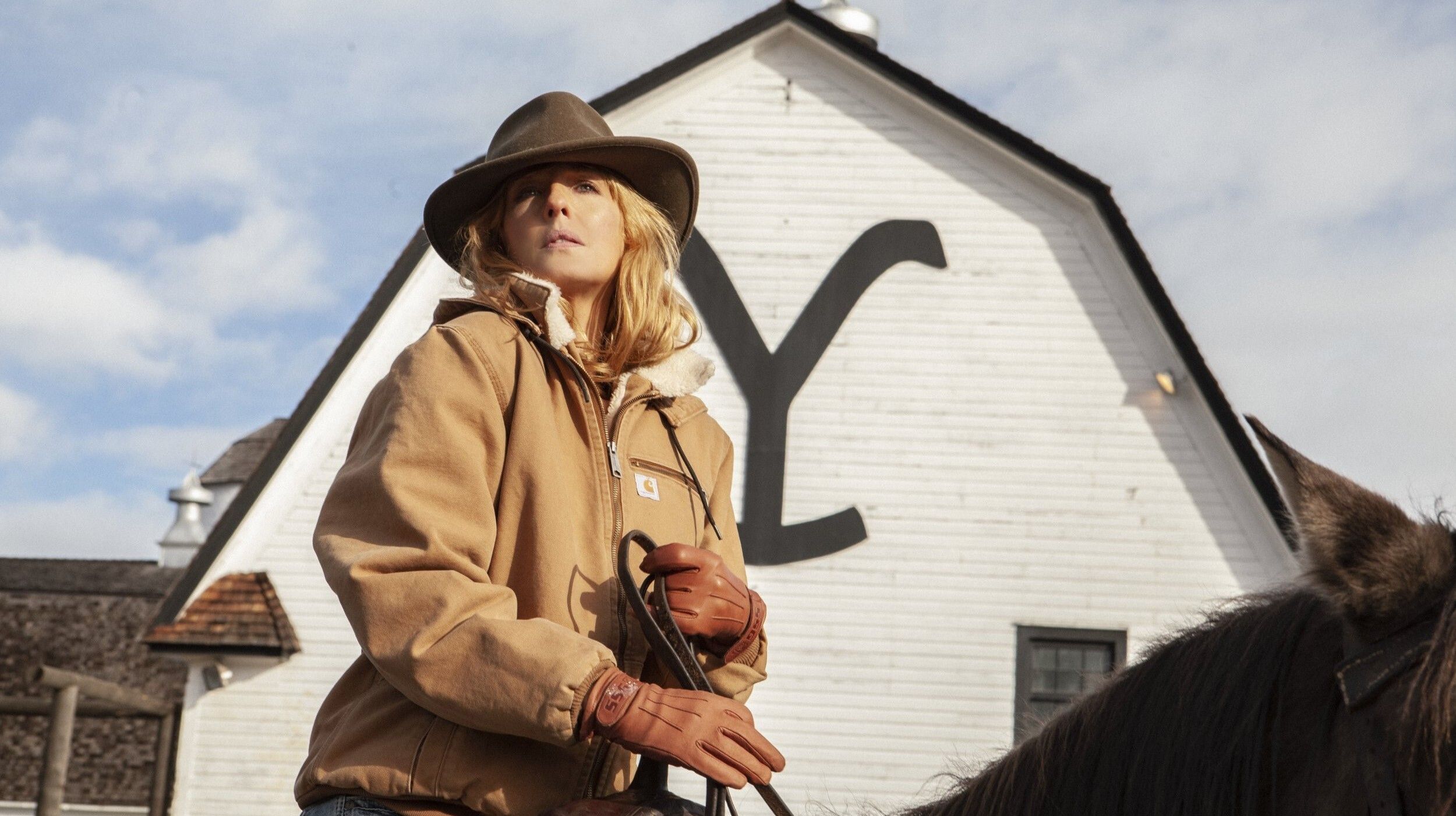 Kelly Reilly as Beth Dutton riding a horse in front of the Yellowstone ranch in Yellowstone