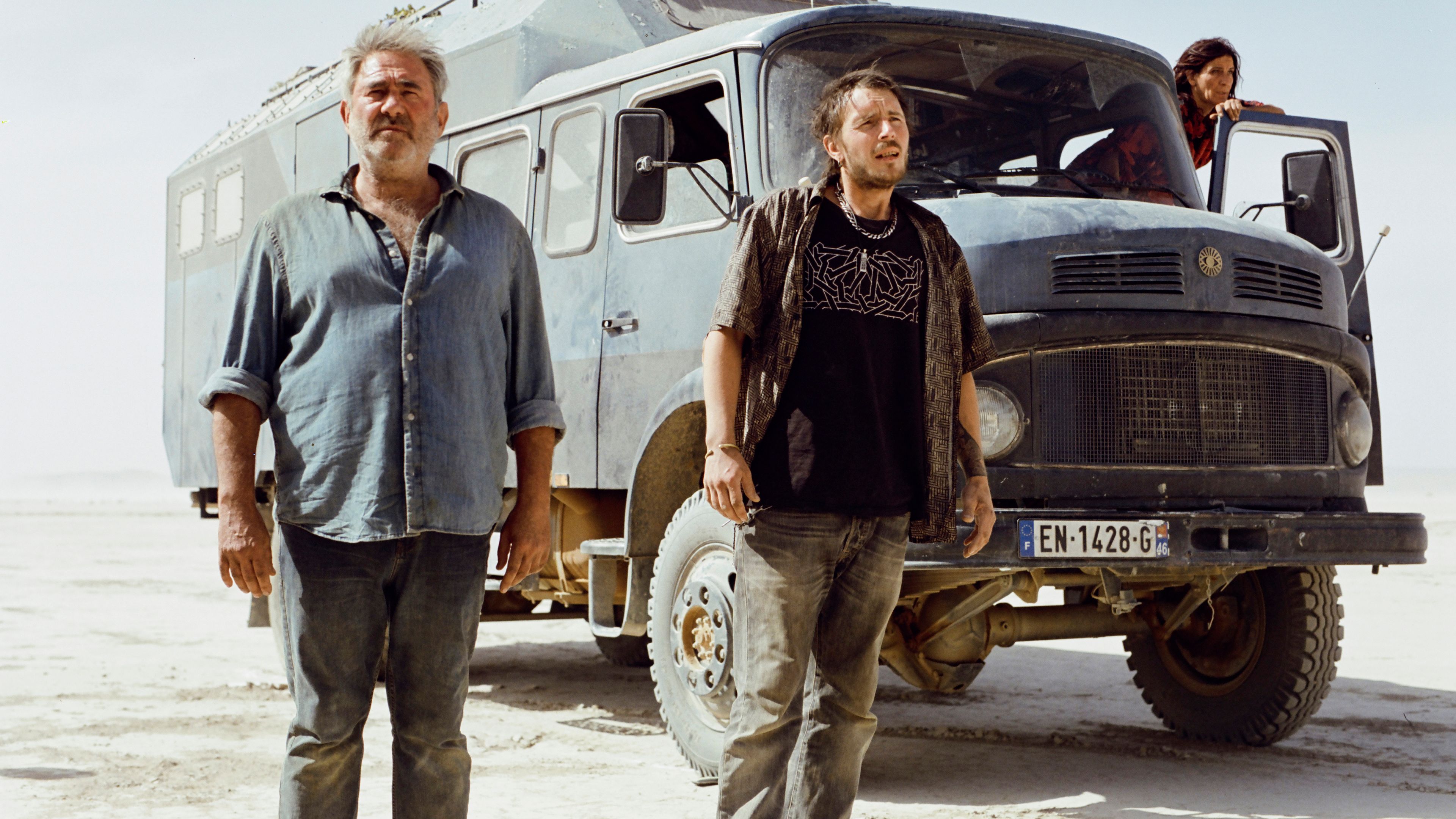 A group of people standing in front of a truck looking worried in the desert in Sirat