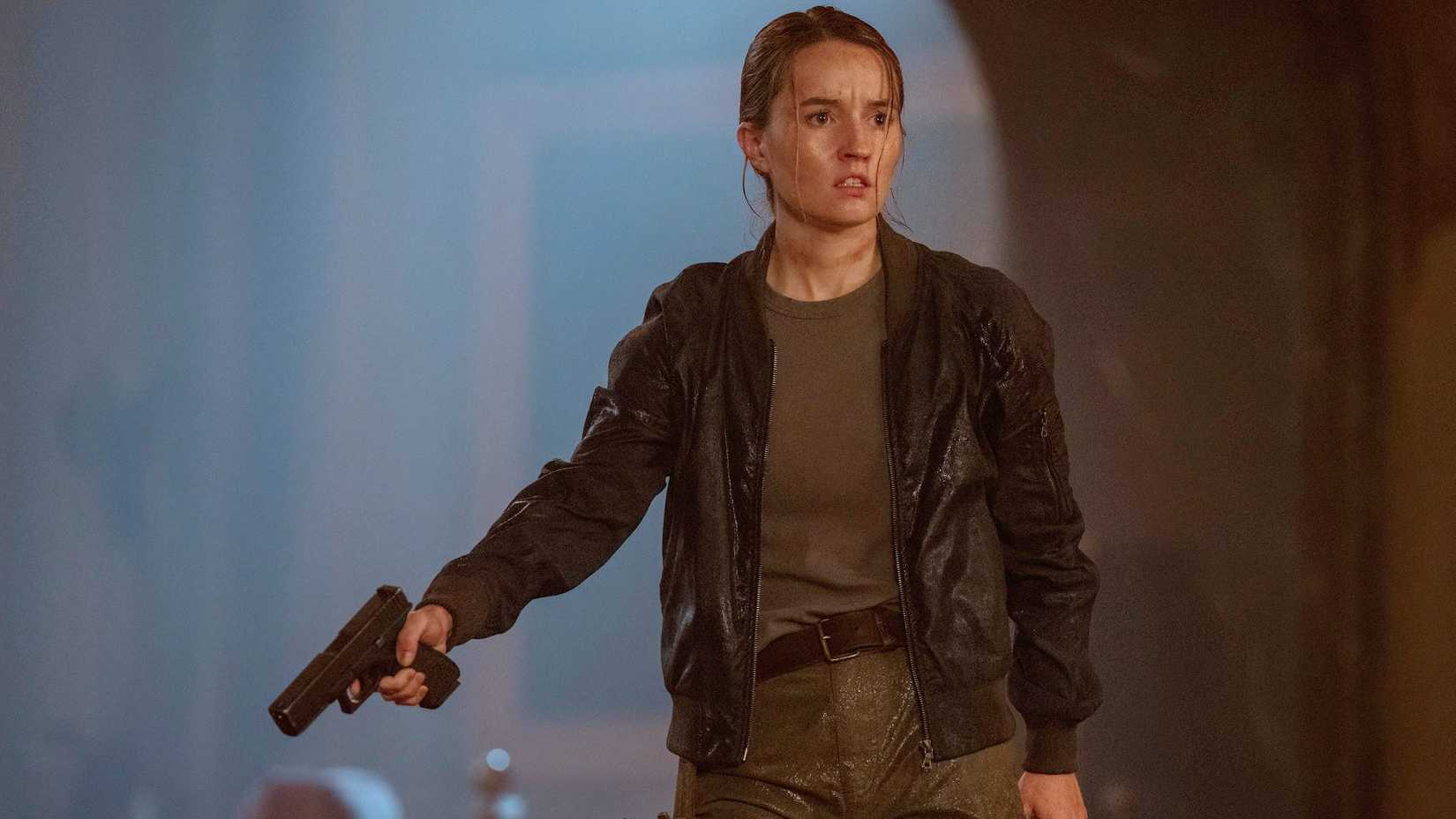 Kaitlyn Dever como Abby em The Last of Us apontando uma arma para baixo enquanto olha para alguém.