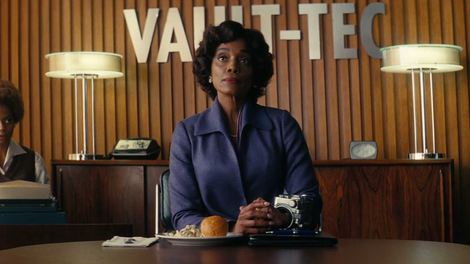 Барб Френс Тернер за столом конференц-зала компании Vault-Tec с едой перед собой в Fallout, сезон 2