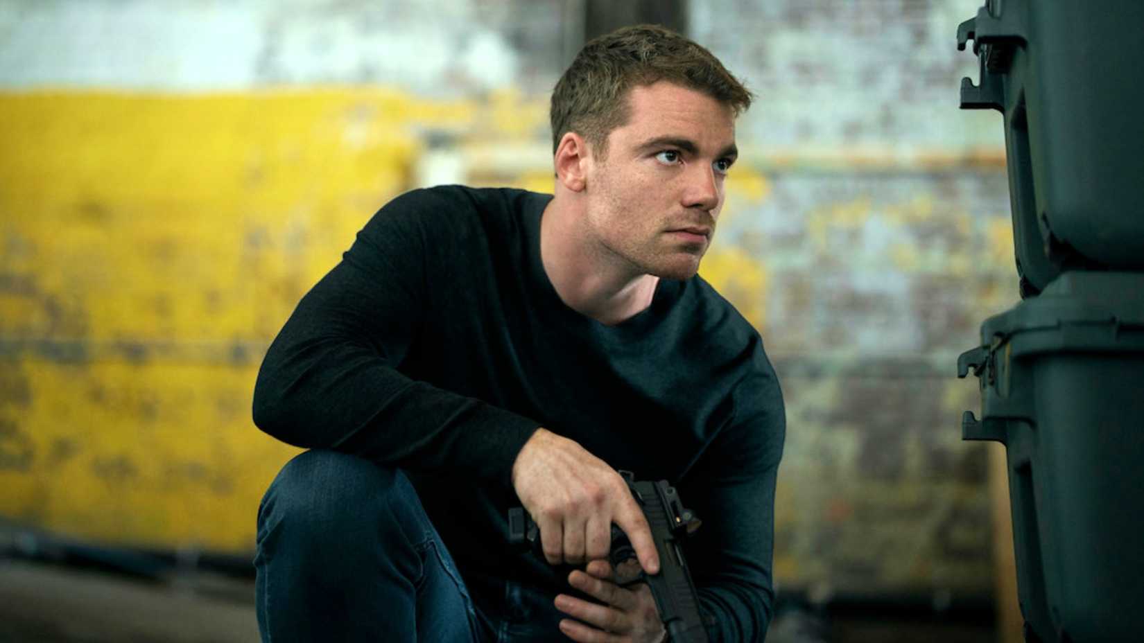 Gabriel Basso as Peter hiding behind boxes in The Night Agent season 3