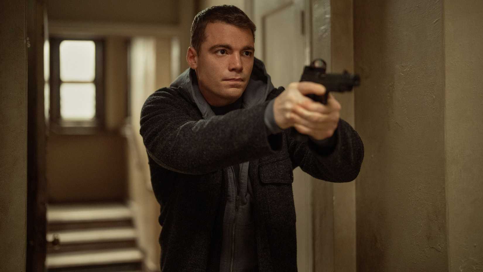 Gabriel Basso plays Peter Sutherland pointing a gun in the hallway in Season 3 of The Night Agent