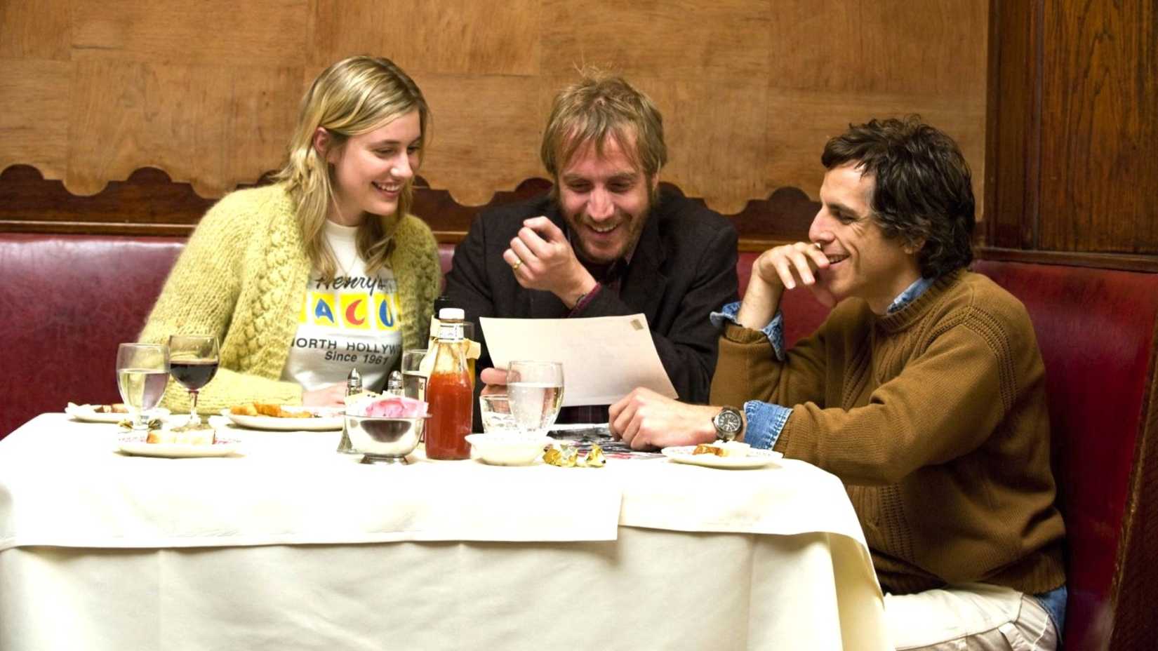 Ben Stiller, Rhys Ifans, and Greta Gerwig look at a paper while sitting at table in Greenberg