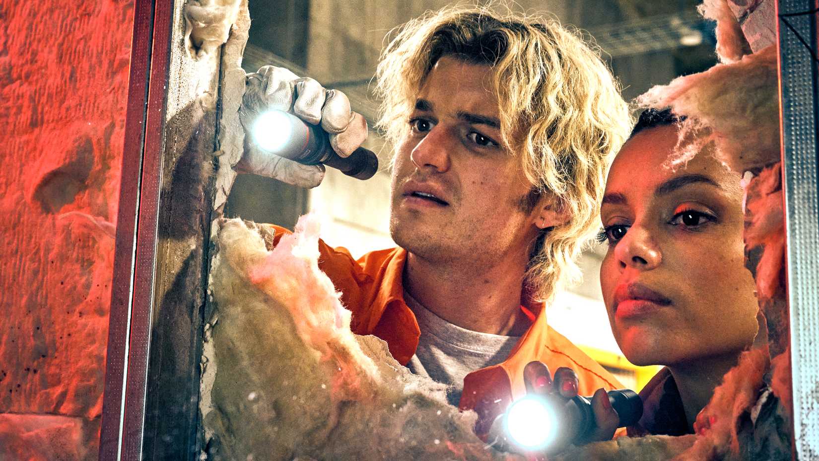 Joe Keery's Teacake and Georgina Campbell's Naomi looking curiously through a hole in the wall in Cold Storage