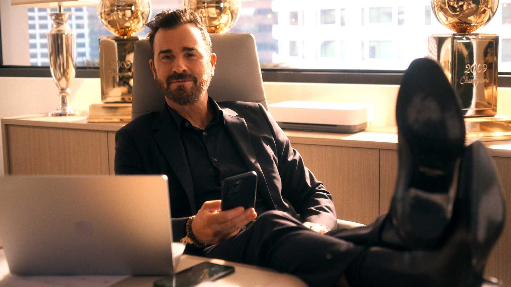 12 Upcoming Netflix Shows You Cannot Miss 8 Justin Theroux's Cam with his feet on his desk and holding his phone in Running Point season 1