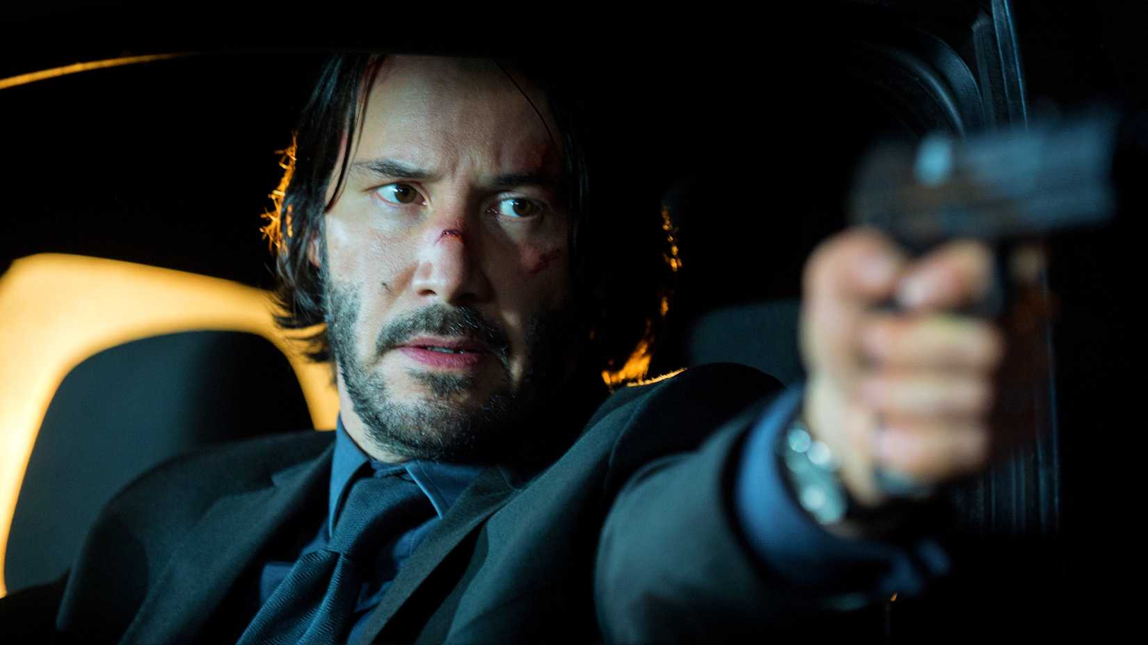 Keanu Reeves segurando uma arma em um carro em John Wick.